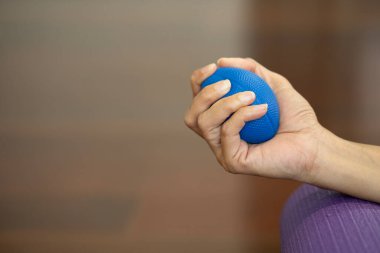 Hands of a woman squeezing a blue stress ball on the yoga mat for work out at home