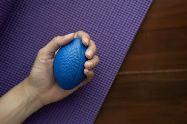 Hands of a woman squeezing a blue stress ball on the yoga mat for work out at home