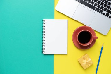 Kahve fincanı, not defteri, bilgisayar sarı ve yeşil masa üzerinde ofis arka planında.