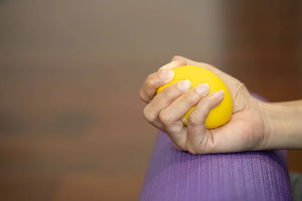 Hands of a woman squeezing a stress ball on the yoga mat.