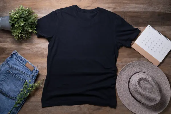 Mockup of a black t-shirt blank shirt template with accessories on the wooden table background, lifestyle and travel concept