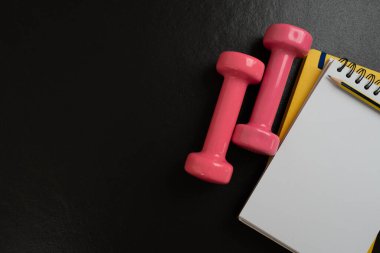 Not defteri ve halter ekipman sporu zamanı siyah arka plan, spor ve sağlıklı konsept.