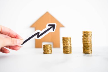 İpotek çıkarları ve gayrimenkul fiyatları kavramsal imajda yükseliyor, karton evin önünde artan bozuk para ve ok yığınları