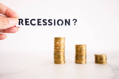 Tasarruf ve kazancın azaltılması sembolü olan bozuk para yığınları önünde soru işareti içeren durgunluk metni