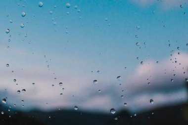 Pencere camına konan yağmur damlalarının arkaplan veya doku görüntüsü ve arkasında odak muantin manzarası var