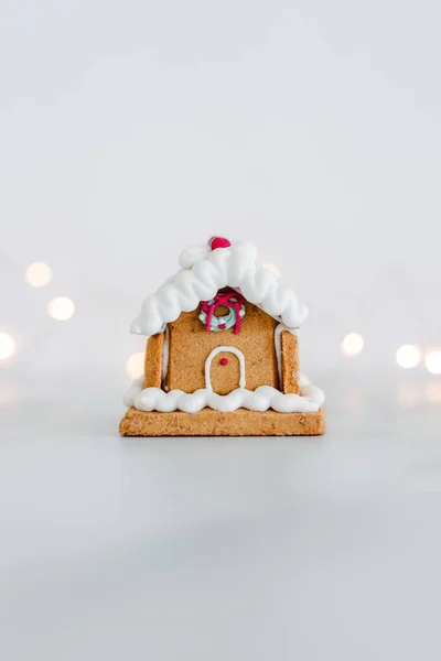 festive Christmas gingerbread house with fairy lights in the background on off white minimalist composition