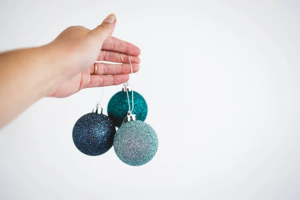 hand holding glittery Christmas baubles with blue and teal tones on white background, concept of festive season and winter holidays