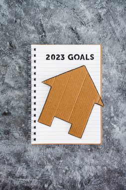 concept of buying a house or settling down, 2023 goals on notebook with cardboard house clipart