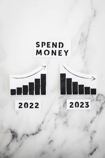 spend money text with 2022 chart showing stats increasing and 2023 graph showing stats decreasing, concept of consumer spending going down in the new year