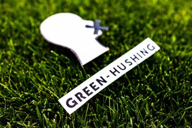 green-hushing concept about companies staying silent about their environmental footprints and policies, text and face with  mouth shut on green grass