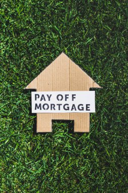 financial independence and being free from debt, Pay Off Mortgage text over cardboard house on perfect green lawn shot under strong sunshine clipart