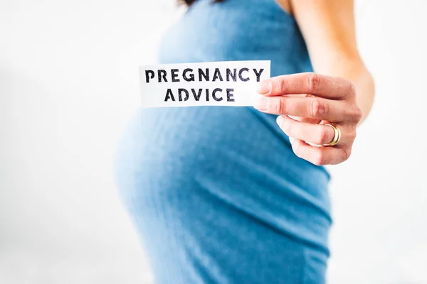 pregnant woman holding Pregnancy Advice sign towards the camera wearing blue dress in the last month of pregnancy,  shot at shallow depth of field