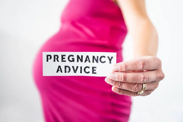 妊娠中の女性妊娠の最後の月にピンクのドレスを着てカメラに向かってアドバイスサインを保持します フィールドの浅い深さで撮影 ロイヤリティフリーのストック画像