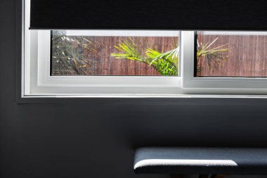 Pencerenin yarısı kör, dışarıdaki tropikal arka bahçeyi gösteriyor ve içerideki minimalist iç dekorla, sığ alan derinliğinde çekiliyor, pencereye odaklan.