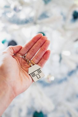 hand holding house keyring in front of white Christmas tree, dream home and home ownership concept clipart