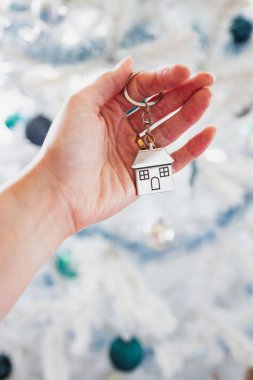 hand holding house keyring in front of white Christmas tree, dream home and home ownership concept clipart