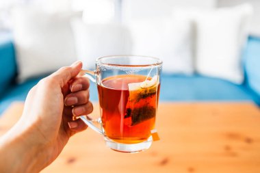 Mavi koltuğun önünde çay poşeti ile birlikte beyaz yastıklı bir fincan rooibos çayı tutarken.