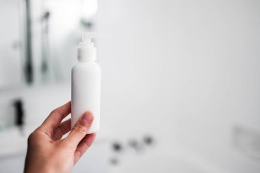 Beyaz banyo arka planında el ele tutuşan nemlendirici vücut losyonu şişesi. Günlük cilt bakımı kavramı.
