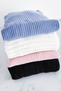 Farklı renkte örgü ve süveter yığını düzgünce katlanmış ve minimalist arka planda birikmiş.