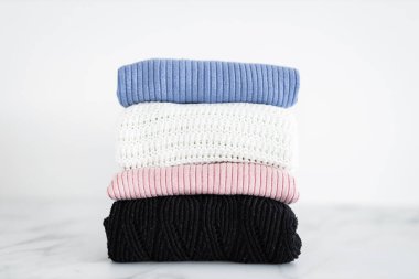 Farklı renkte örgü ve süveter yığını düzgünce katlanmış ve minimalist arka planda birikmiş.