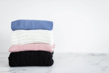 Farklı renkte örgü ve süveter yığını düzgünce katlanmış ve minimalist arka planda birikmiş.