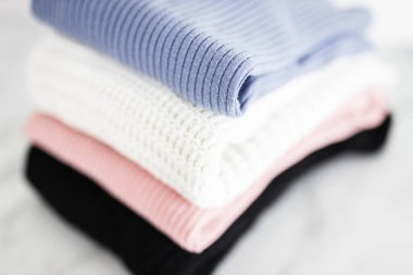 Farklı renkte örgü ve süveter yığını düzgünce katlanmış ve minimalist arka planda birikmiş.