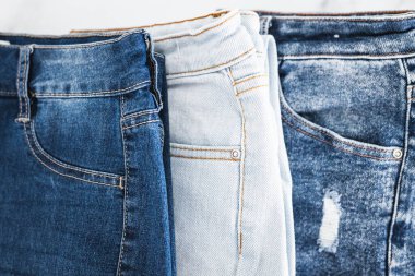 Farklı renk kot kumaşlı kot pantolon yığını düzgünce katlandı ve minimalist arka planda yığıldı