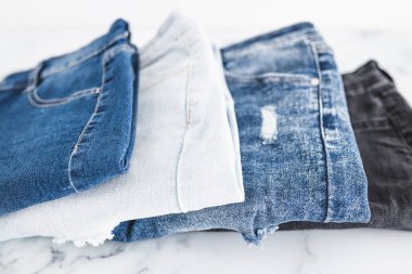 Farklı renk kot kumaşlı kot pantolon yığını düzgünce katlandı ve minimalist arka planda yığıldı