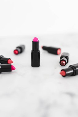 Gösteriş masasına saçılmış renkli ruj grupları, minimalist zarif mermer arka plan, aşırı sığ alan derinliği
