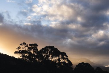 Tazmanya, Avustralya 'daki dağların üzerinde güneş ışığı ve bulutlarla dolu güzel bir günbatımı gökyüzü.