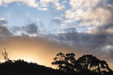 Tazmanya, Avustralya 'daki dağların üzerinde güneş ışığı ve bulutlarla dolu güzel bir günbatımı gökyüzü.