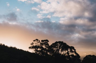 Tazmanya, Avustralya 'daki dağların üzerinde güneş ışığı ve bulutlarla dolu güzel bir günbatımı gökyüzü.