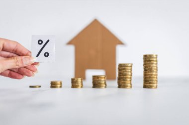 interest rates for loans and mortgages going up conceptual image, percentage symbol with growing stacks of coins representing increasingly expensive cost of financing in front of cardboard house