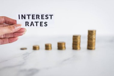 Interest Rates text with growing stacks of coins representing increasingly expensive loans and mortgages, concept of global economy struggling after the covid-19 pandemic