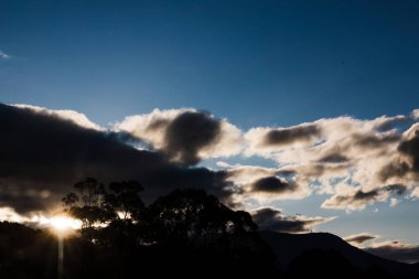 Tazmanya 'daki dağların üzerinde dramatik bir günbatımı. Koyu bulutlar, mavi gökyüzü, parlayan güneş ışınları ve parlayan merceklerle.