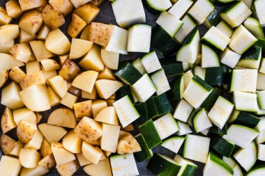 Fırın tepsisindeki küçük küplerde doğranmış bebek patatesler ve kabak. Basit bir ev yapımı tabakta kızartılmaya hazır.