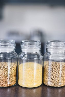 İçinde kinoa mercimek, karabuğday ve arpanın da bulunduğu farklı türde tahıl ve baklagillerin bulunduğu açık kiler kavanozları mutfak tezgahı, basit malzeme konsepti.