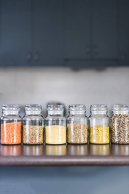 İçinde kinoa mercimek, karabuğday ve arpanın da bulunduğu farklı türde tahıl ve baklagillerin bulunduğu açık kiler kavanozları mutfak tezgahı, basit malzeme konsepti.