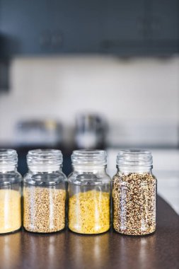 İçinde kinoa mercimek, karabuğday ve arpanın da bulunduğu farklı türde tahıl ve baklagillerin bulunduğu açık kiler kavanozları mutfak tezgahı, basit malzeme konsepti.