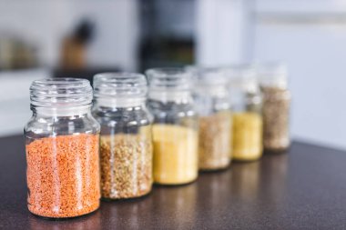 İçinde kinoa mercimek, karabuğday ve arpanın da bulunduğu farklı türde tahıl ve baklagillerin bulunduğu açık kiler kavanozları mutfak tezgahı, basit malzeme konsepti.