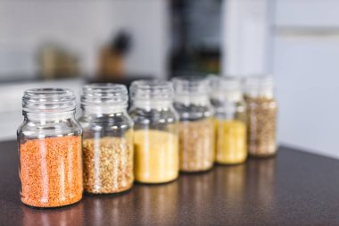 İçinde kinoa mercimek, karabuğday ve arpanın da bulunduğu farklı türde tahıl ve baklagillerin bulunduğu açık kiler kavanozları mutfak tezgahı, basit malzeme konsepti.