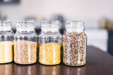 İçinde kinoa mercimek, karabuğday ve arpanın da bulunduğu farklı türde tahıl ve baklagillerin bulunduğu açık kiler kavanozları mutfak tezgahı, basit malzeme konsepti.