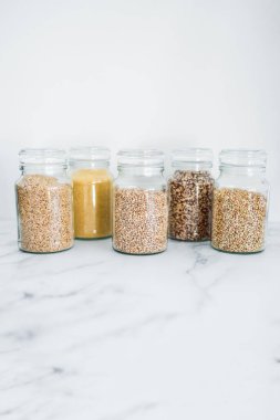 İçinde kinoa pirinç karabuğday kuskusu ve arpa da dahil olmak üzere içinde farklı tahıl türleri bulunan temiz kiler kavanozları, basit doğal sağlıklı bileşenler kavramı.