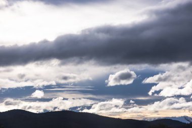 Güneş ışığı, karanlığı ve beyaz bulutları aşarak Tazmanya dağlarının üzerinden geçiyor. Tamamen zıtlık ve doğal güzellikle dolu.