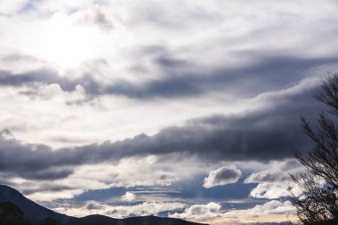 Güneş ışığı, karanlığı ve beyaz bulutları aşarak Tazmanya dağlarının üzerinden geçiyor. Tamamen zıtlık ve doğal güzellikle dolu.