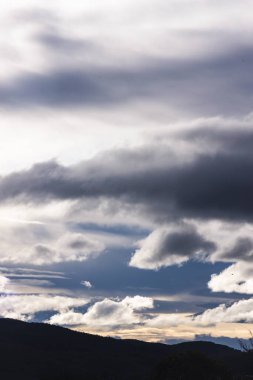 Güneş ışığı, karanlığı ve beyaz bulutları aşarak Tazmanya dağlarının üzerinden geçiyor. Tamamen zıtlık ve doğal güzellikle dolu.