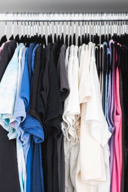 Birbirine uyumlu askıları ve tişörtleri, tişörtleri, kazakları, ev temasını içeren renklendirilmiş tişörtleri olan düzenli bir gardırop.