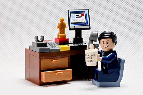 stock image Osaka, Japan - February 19, 2023 Lego businessman sits at his working table with computer, trophy, cup and telephone receiver on white dot color background.