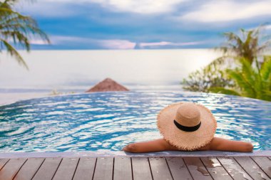 Yüzme havuzunda şapkalı bir kadın önünde mavi gökyüzü olan denize bakıyor. Yaz konsepti.