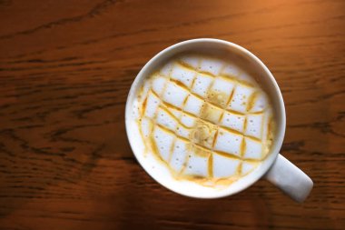 Tahta arka plandaki beyaz fincanda sıcak karamel macchiato kahvesi. İçki konsepti.